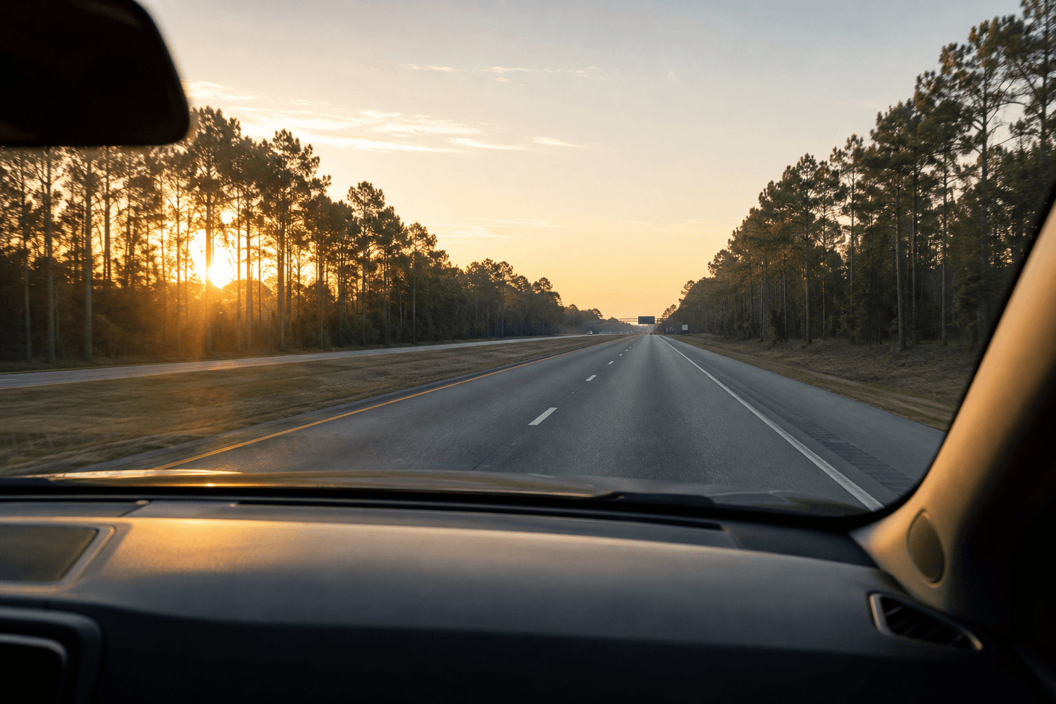 View of a sunrise commute on a highway lined with pine trees near The Woodlands, Texas