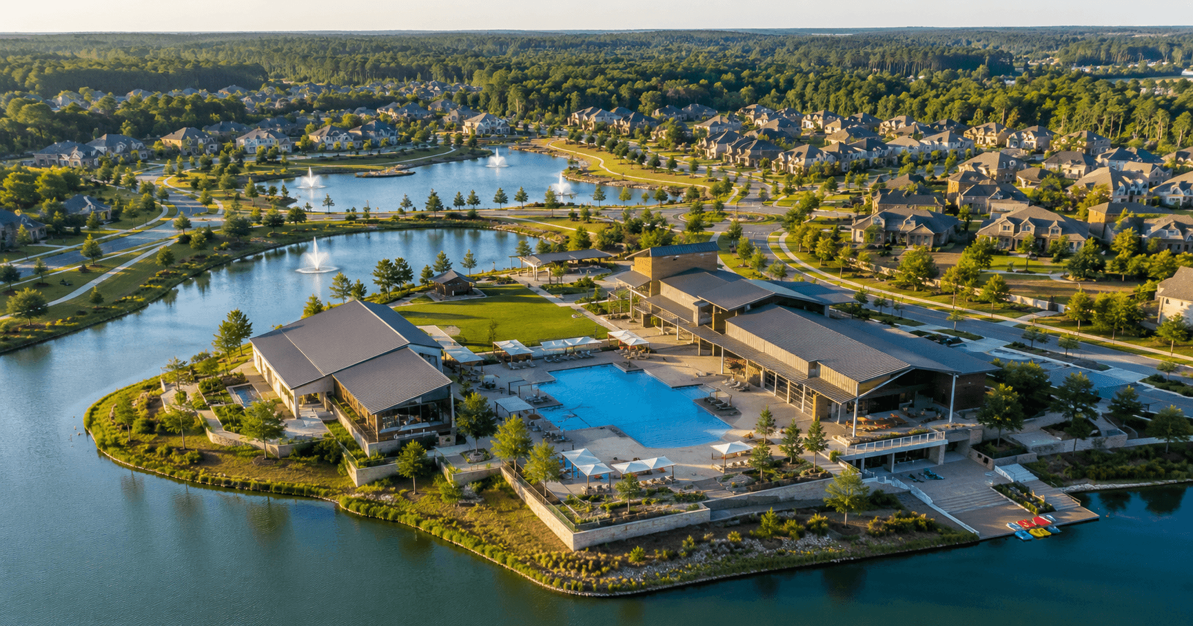 Aerial view of Artavia community in Conroe Texas with resort amenity center, lagoon pools, and multiple lakes at golden hour